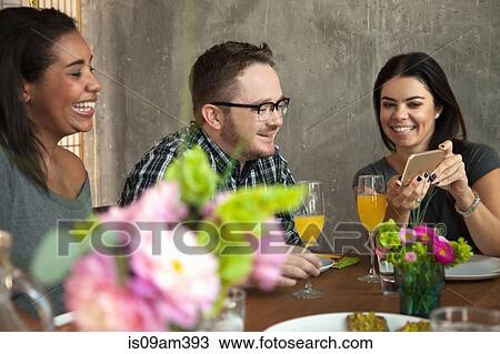 "Friends at dinner table, young woman showing friend smartphone screen" View Large Photo Image Stock Image - "Friends at dinner table, young woman showing friend smartphone screen". Fotosearch