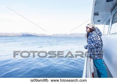 Stock Image - "Girl leaning against railing on boat sailing toward coast, Ushuaia, Tierra del Fuego, Argentina". Fotosearch