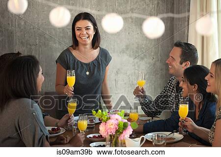 Stock Image - "Group of friends at dinner table, young woman making toast". Fotosearch