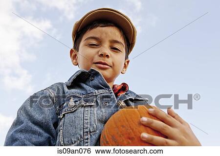 Stock Photograph - Low angle portrait of boy holding pumpkin. Fotosearch
