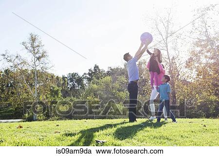 Stock Image - Mature couple and children playing catch with ball in park. Fotosearch