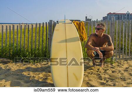 Mature male surfer crouching with surfboard at beach View Large Photo Image Stock Photo - Mature male surfer crouching with surfboard at beach. Fotosearch