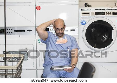 Mature man in surgical scrubs using digital tablet in laundry room View Large Photo Image Stock Photo - Mature man in surgical scrubs using digital tablet in laundry room. Fotosearch