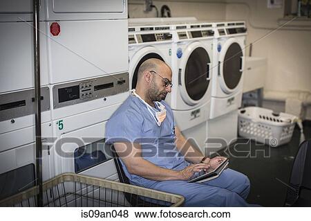 Mature man in surgical scrubs using touchscreen on digital tablet in laundry room View Large Photo Image Stock Photo - Mature man in surgical scrubs using touchscreen on digital tablet in laundry room. Fotosearch