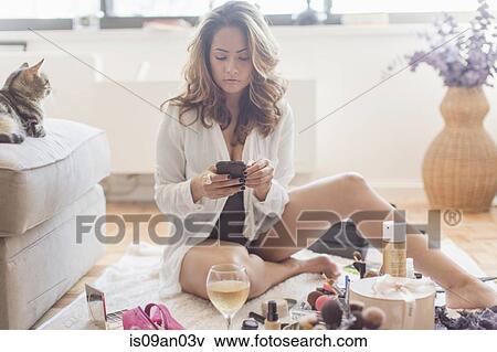 Mid adult woman texting on smartphone whilst getting ready in living room View Large Photo Image Stock Photo - Mid adult woman texting on smartphone whilst getting ready in living room. Fotosearch