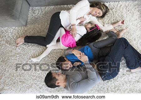 Stock Image - Overhead view of mature couple and two children play fighting on living room floor. Fotosearch
