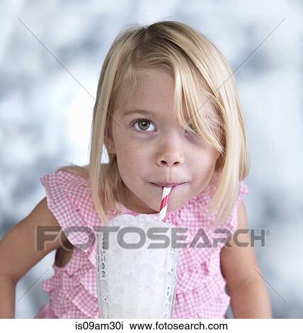 Stock Image - Portrait of cute female toddler blowing bubbles in glass of milk. Fotosearch