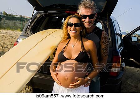 Portrait of mature male surfer embracing pregnant wife at beach View Large Photo Image Stock Photo - Portrait of mature male surfer embracing pregnant wife at beach. Fotosearch