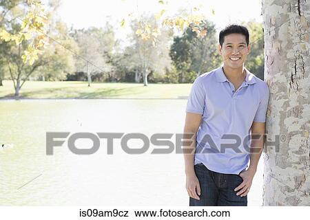Stock Photo - Portrait of mature man leaning against tree in park. Fotosearch