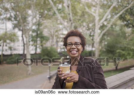 Portrait of smiling mature woman drinking takeaway coffee in park View Large Photo Image Picture - Portrait of smiling mature woman drinking takeaway coffee in park. Fotosearch