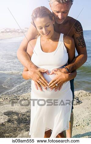 Pregnant mature woman and husband making heart shape on stomach at beach View Large Photo Image Stock Photography - Pregnant mature woman and husband making heart shape on stomach at beach. Fotosearch