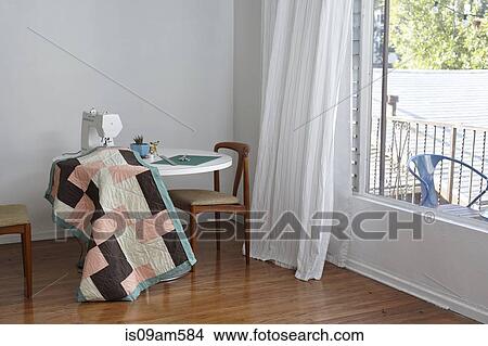 Picture - Quilt in sewing machine on table by window. Fotosearch