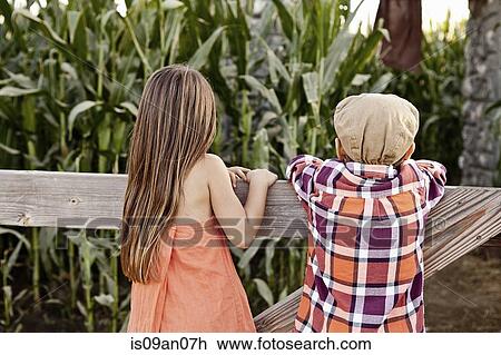 Rear view of boy and girl leaning against field fence View Large Photo Image Stock Image - Rear view of boy and girl leaning against field fence. Fotosearch