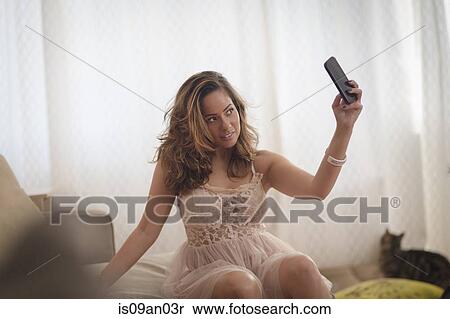 Stock Photography - Sexy mid adult woman taking smartphone selfie on living room sofa. Fotosearch