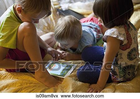 Stock Photo - Three young children relaxing on bed using digital tablet. Fotosearch