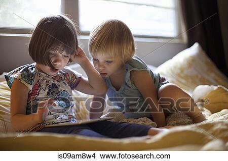 Three young girls sitting on bed using digital tablet View Large Photo Image Picture - Three young girls sitting on bed using digital tablet. Fotosearch