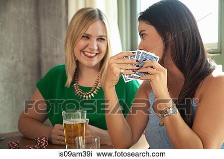 Stock Image - "Two female friends playing cards, and laughing, at table". Fotosearch