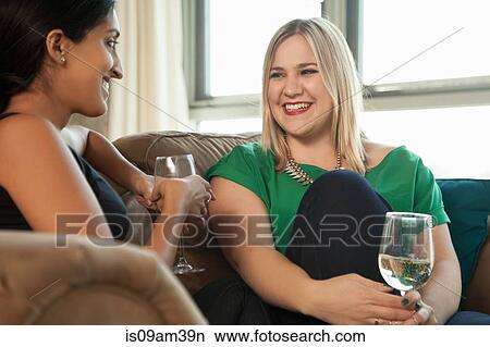 Picture - "Two female friends sitting on sofa, drinking wine". Fotosearch
