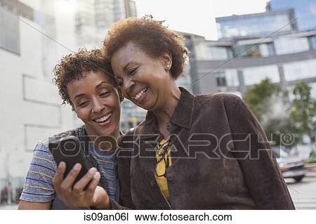 Two mature female friends laughing at smartphone texts on street View Large Photo Image Stock Image - Two mature female friends laughing at smartphone texts on street. Fotosearch