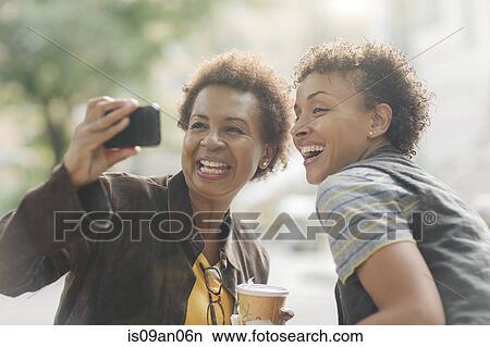 Picture - Two mature female friends taking smartphone selfie on street. Fotosearch