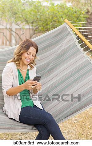 Stock Image - Woman using smartphone on hammock. Fotosearch