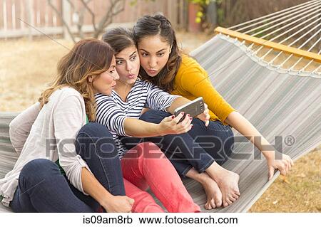 Stock Image - Women taking selfie with smartphone on hammock. Fotosearch