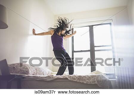 Stock Photography - Young Asian woman dancing on bed. Fotosearch