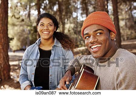 Stock Photo - Young camping couple sitting in forest playing acoustic guitar. Fotosearch