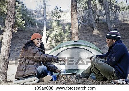 Stock Photo - Young camping couple sitting in forest laughing and chatting. Fotosearch