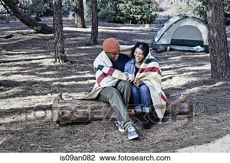 Young camping couple sitting on log wrapped in blanket View Large Photo Image Stock Image - Young camping couple sitting on log wrapped in blanket. Fotosearch