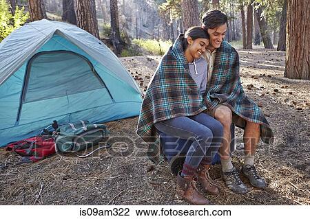 Stock Image - "Young camping couple wrapped in blanket in forest, Los Angeles, California, USA". Fotosearch