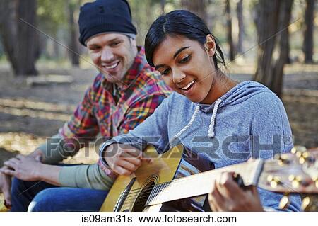 Stock Photograph - "Young couple in forest playing acoustic guitar, Los Angeles, California, USA". Fotosearch