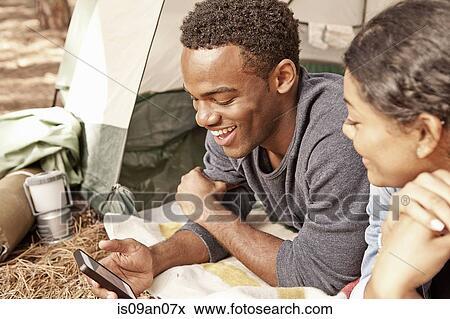 Stock Photo - Young couple lying in tent entrance reading smartphone texts. Fotosearch