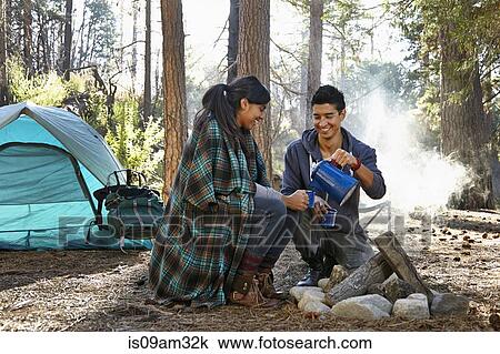 Stock Image - "Young couple pouring coffee by campfire in forest, Los Angeles, California, USA". Fotosearch