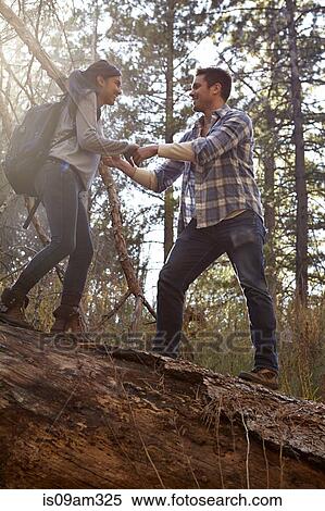 Stock Photography - "Young man giving girlfriend a helping hand on fallen tree in forest, Los Angeles, California, USA". Fotosearch