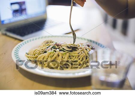 "Young woman at table eating plate of noodles, focus on food" View Large Photo Image Picture - "Young woman at table eating plate of noodles, focus on food". Fotosearch