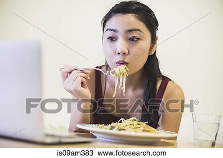 Young woman at table eating plate of noodles View Large Photo Image Stock Image - Young woman at table eating plate of noodles. Fotosearch