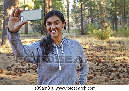 Stock Photograph - "Young woman in forest taking smartphone selfie, Los Angeles, California, USA". Fotosearch