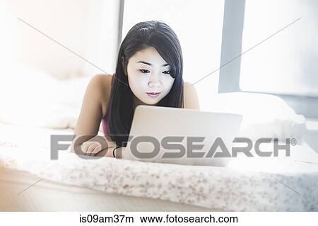 "Young woman lying on bed, using laptop" View Large Photo Image Picture - "Young woman lying on bed, using laptop". Fotosearch
