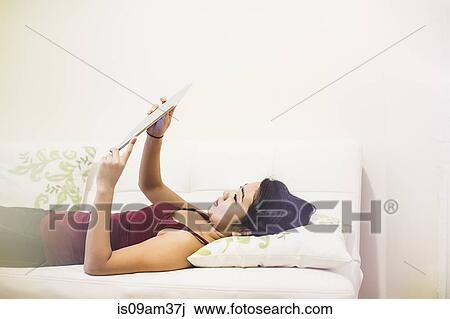 "Young woman lying on sofa, using digital tablet" View Large Photo Image Stock Image - "Young woman lying on sofa, using digital tablet". Fotosearch