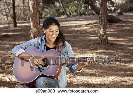 Young woman sitting in forest playing acoustic guitar View Large Photo Image Stock Image - Young woman sitting in forest playing acoustic guitar. Fotosearch