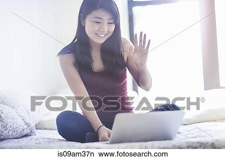 "Young woman sitting on bed, using laptop for video call" View Large Photo Image Picture - "Young woman sitting on bed, using laptop for video call". Fotosearch
