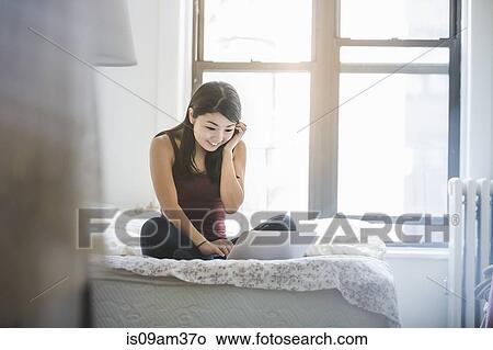 "Young woman sitting on bed, using laptop for video call" View Large Photo Image Picture - "Young woman sitting on bed, using laptop for video call". Fotosearch