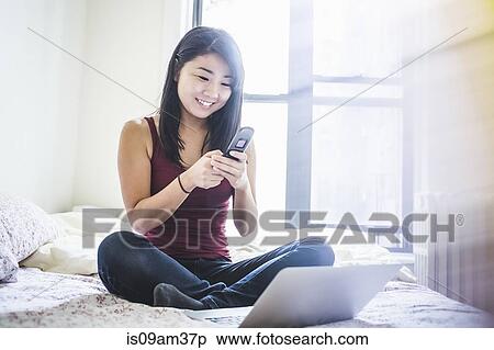 "Young woman sitting on bed, using smartphone and laptop for video call" View Large Photo Image Stock Photography - "Young woman sitting on bed, using smartphone and laptop for video call". Fotosearch