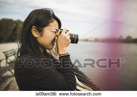 Stock Image - "Young woman taking photographs, outdoors". Fotosearch