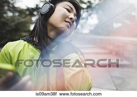Stock Image - "Young woman wearing headphones, listening to music, outdoors". Fotosearch