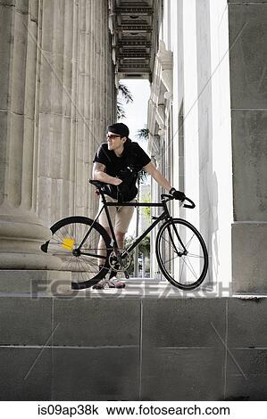 Stock Image - Bike messenger taking break beside column. Fotosearch