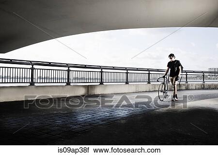 Stock Image - "Bike messenger walking, pushing bike". Fotosearch