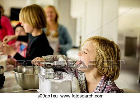 Stock Photograph - Boy eating icing sugar from spatula in kitchen. Fotosearch