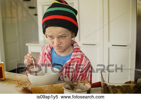 Stock Photography - Boy pulling face whilst mixing cake in kitchen. Fotosearch